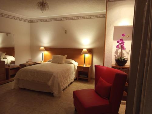 a hotel room with a bed and a red chair at Casa Brasa, Sol & Jardín in Guanajuato