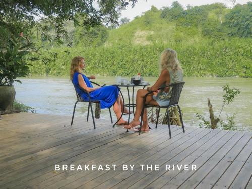 two women sitting at a table next to a river at Nómada Tayrona - Riverside Suites in Los Naranjos