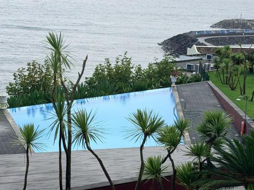 a swimming pool next to the ocean with palm trees at Marina Mar II - Moradia T3 in Vila Franca do Campo