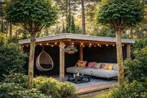a pergola with a couch and a hammock in a garden at StayatSas Pippa grote omheinde tuin in het bos aan grote vijver, zwembad en restaurant op het park, stijlvol ingericht,veel privacy in Doornspijk