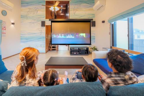 a family sitting in a living room watching tv at まるで映画館 本格シアター 寝室6部屋 大家族大集合 海まで徒歩すぐ ---オーシャニア一宮--- in Ichinomiya