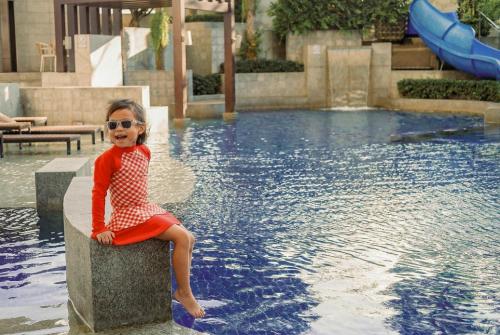 a little girl sitting on a block in front of a swimming pool at Jasmine Grande Residence Suite Bangkok in Bangkok