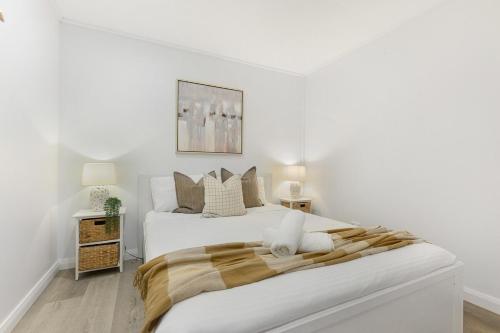 a white bedroom with a large white bed and two lamps at Collaroy 3Br Beach Home with Large Pool Ground Floor in Collaroy
