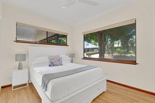 a white bedroom with a bed and two windows at Balu luxe in Broome
