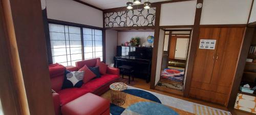 a living room with a red couch and a piano at Suzume no oyado SO1 in Shima
