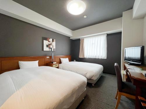 a hotel room with two beds and a desk and a television at Hotel Route-Inn Mikawa Inter in Hakusan