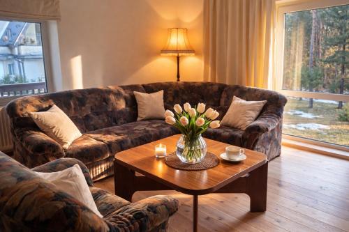 a living room with a couch and a table with flowers at Pamiškės Villa in Kulautuva
