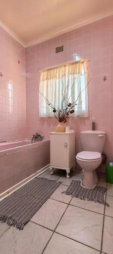 a pink bathroom with a toilet and a tub at Marli Guesthouse Self-Catering in Welkom