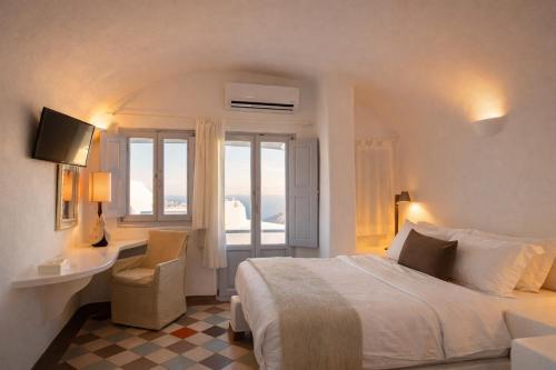 a bedroom with a bed and a desk and a window at Ikastikies Suites in Firostefani