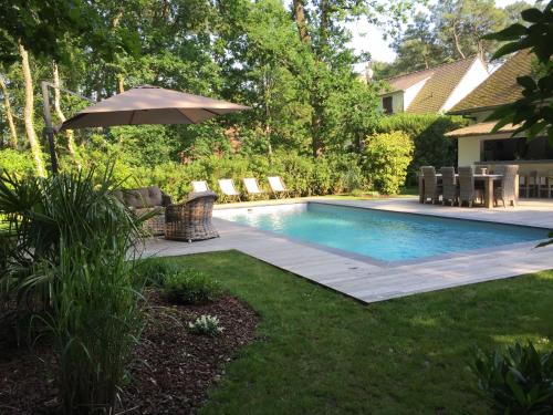 uma piscina com um guarda-sol ao lado de um quintal em Villa d'hôtes Graine de Pin em Le Touquet-Paris-Plage