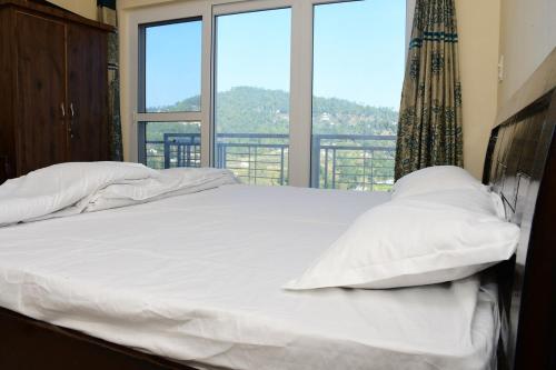 a bed with white sheets and pillows in front of a window at Serenidad- The Cottage in Mukteshwar