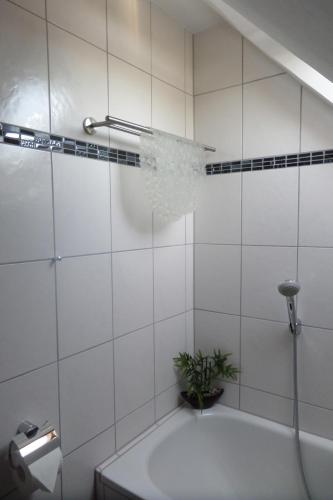 a white tiled bathroom with a tub and a plant at Flughafenapartement Sky View in Düsseldorf