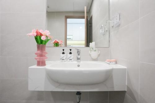 a white bathroom with a sink and a vase of pink flowers at STUDIO Vinhomes Grand Park , thành phố Hồ Chí Minh in Long Bình