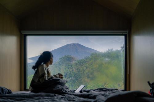 a woman sitting on a bed looking out a window at Bobocabin Gunung Rinjani, Lombok in Sembalun Lawang