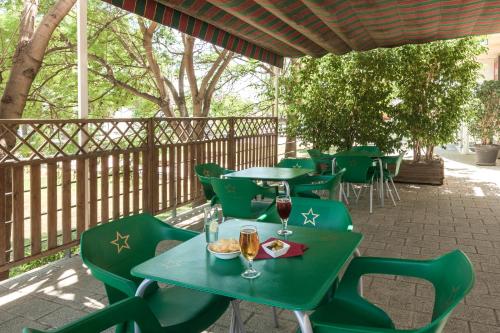 a patio with green tables and chairs with glasses of wine at Ibis Murcia in Murcia
