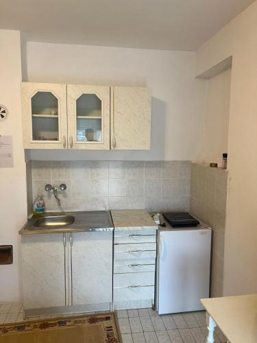 a kitchen with white cabinets and a sink and a refrigerator at Apartmani Palma in Sutomore