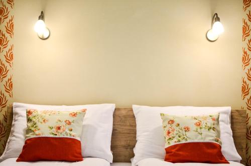 two pillows on a bed with two lights on the wall at Páva Apartmanház in Makó