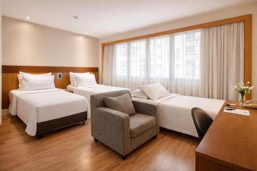 a hotel room with two beds and a chair at Transamerica Executive Faria Lima in São Paulo