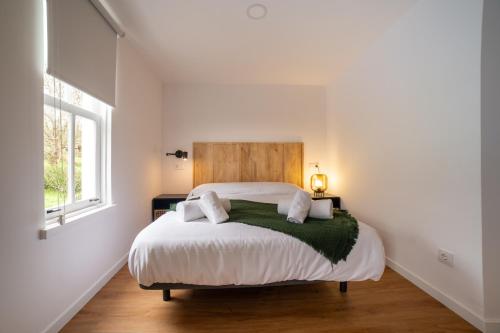 a white bedroom with a large bed with a green blanket at Sarridal, Lar Atlántico in Cedeira
