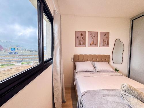 a bedroom with a bed and a large window at Flat moderno com churrasqueira próximo à Unifebe in Brusque