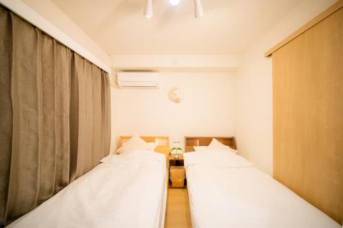 two beds in a small room with a window at HARERUYA Inn SHINJUKU in Tokyo