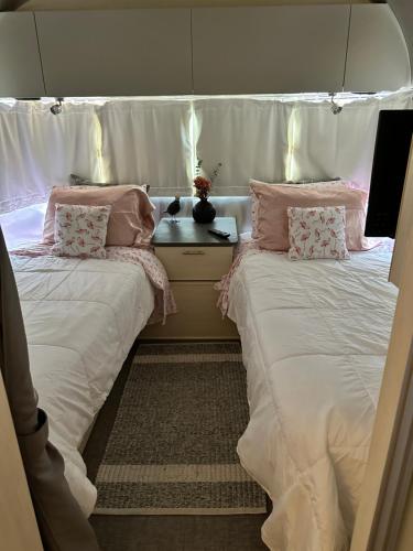 two beds in a room with white sheets and pink pillows at Airstream Alfresco in Fredericksburg