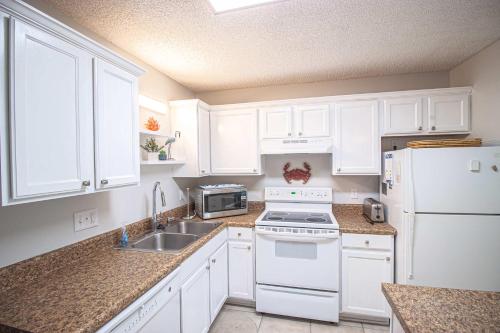 a kitchen with white cabinets and a stove and a sink at Salty Dune 2BR Beach Condo w Pools in Gulf Shores