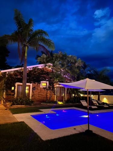 a swimming pool with an umbrella next to a house at Pousada Manacá Exclusive Suítes in Rifaina