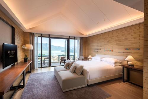 a bedroom with a bed and a tv and a couch at Conrad Hangzhou Tonglu in Yinzhu
