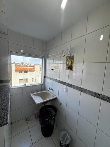 a white tiled bathroom with a sink and a window at Apartamento com varanda in Lavras