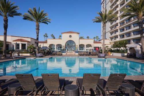 a large swimming pool with chairs and palm trees at The Waterfront Beach Resort, A Hilton Hotel in Huntington Beach