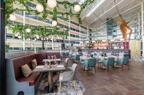 a restaurant with tables and chairs and plants at Hilton London Heathrow Airport in Hillingdon