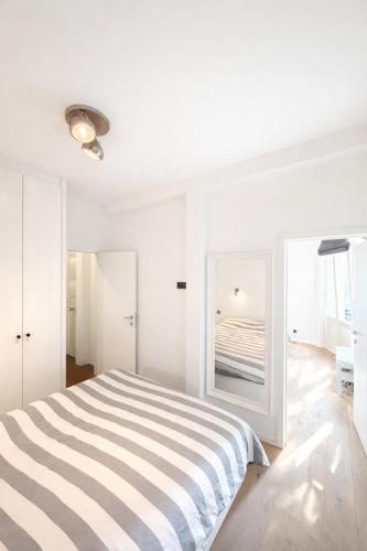 a white bedroom with a striped bed and a mirror at The White Boutique Loft in Antwerp