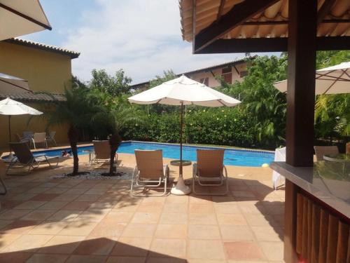 une terrasse avec des chaises et un parasol ainsi qu'une piscine dans l'établissement Condomínio Solar dos Peixes, à Praia do Forte