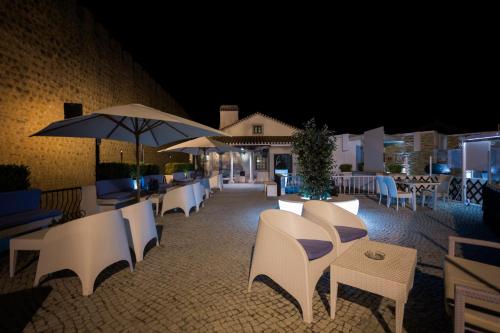 a patio with chairs and tables and umbrellas at night at Josefa D`Obidos Hotel in Óbidos