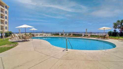 a swimming pool with tables and umbrellas and the ocean at 513 Seascape by AvantStay Oceanfront Home w Amazing Views Community Pool Access in Isle of Palms