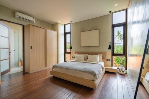 a bedroom with a bed and some windows at Unwind Villa by Betterplace in Canggu