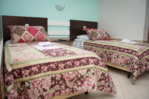 two beds in a hotel room with pink and green blankets at Pousada Theisen in Gramado