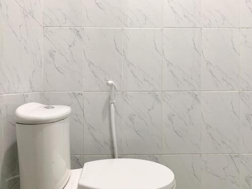 a white toilet in a bathroom with white tiles at Urbanview Hotel The Corner Pandowo in Ngaglik