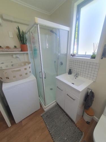 a white bathroom with a shower and a sink at Stanmore Bay Beachfront Cottage in Whangaparaoa