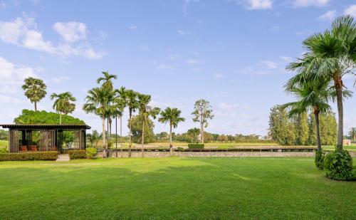 a green yard with a gazebo and palm trees at Hilton Bangkok Suvarnabhumi Golf Resort & Spa in Lat Krabang