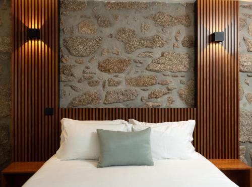 a bedroom with a stone wall and a bed with white pillows at O Paraíso do Sobreiro - Country House in Travanca de Lagos