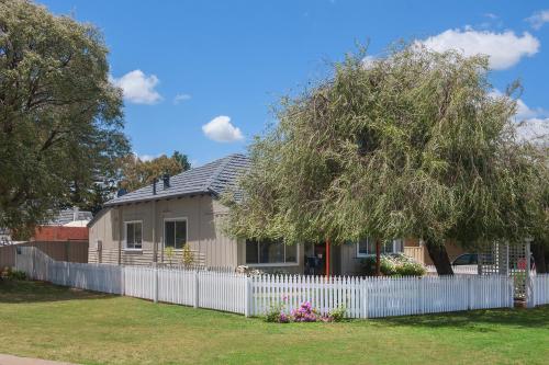 a house with a white fence and a tree at Sea La Vie in Busselton
