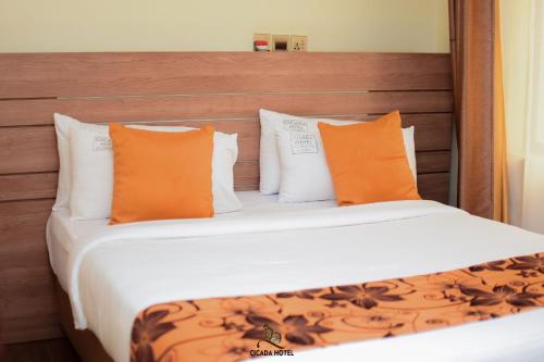ein Schlafzimmer mit einem Bett mit orangefarbenen und weißen Kissen in der Unterkunft Cicada Hotel in Eldoret