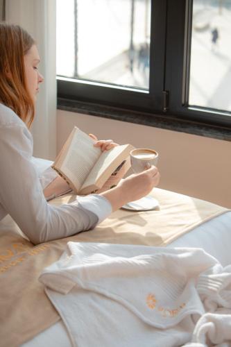 a young girl reading a book while sitting on a bed at Koral Boutique Hotel in Durrës