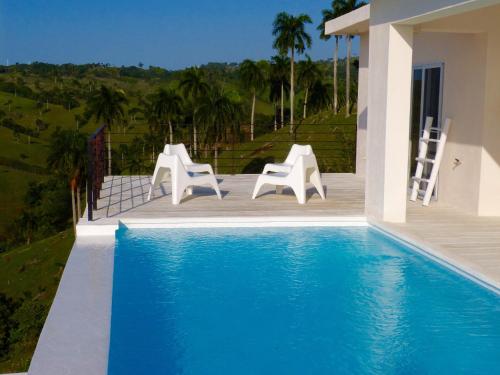 a pool with white chairs and a house at Villa Vertigo in Río San Juan