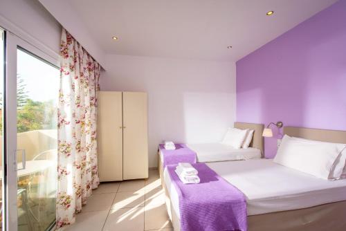 a purple room with two beds and a window at Primavera Beach Hotel Studios & Apartments in Malia