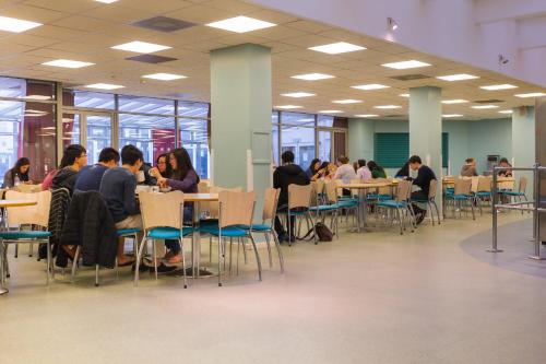 a group of people sitting at tables in a cafeteria at International Hall / University of London in London