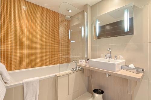 een badkamer met een wastafel, een bad en een spiegel bij Relais De La Malmaison Paris Rueil Hôtel-Spa in Rueil-Malmaison