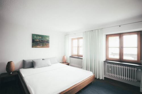 a white bedroom with a bed and two windows at Luna Mia - Apartment 5 in Schwangau